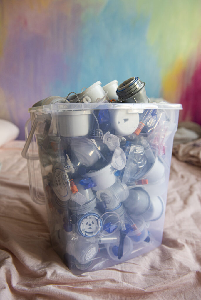 Zdjęcie przedstawia pracę artystki. Kubeł śmieci, odpadów medycznych na kontrastującym, kolorowym i wesołym tle.